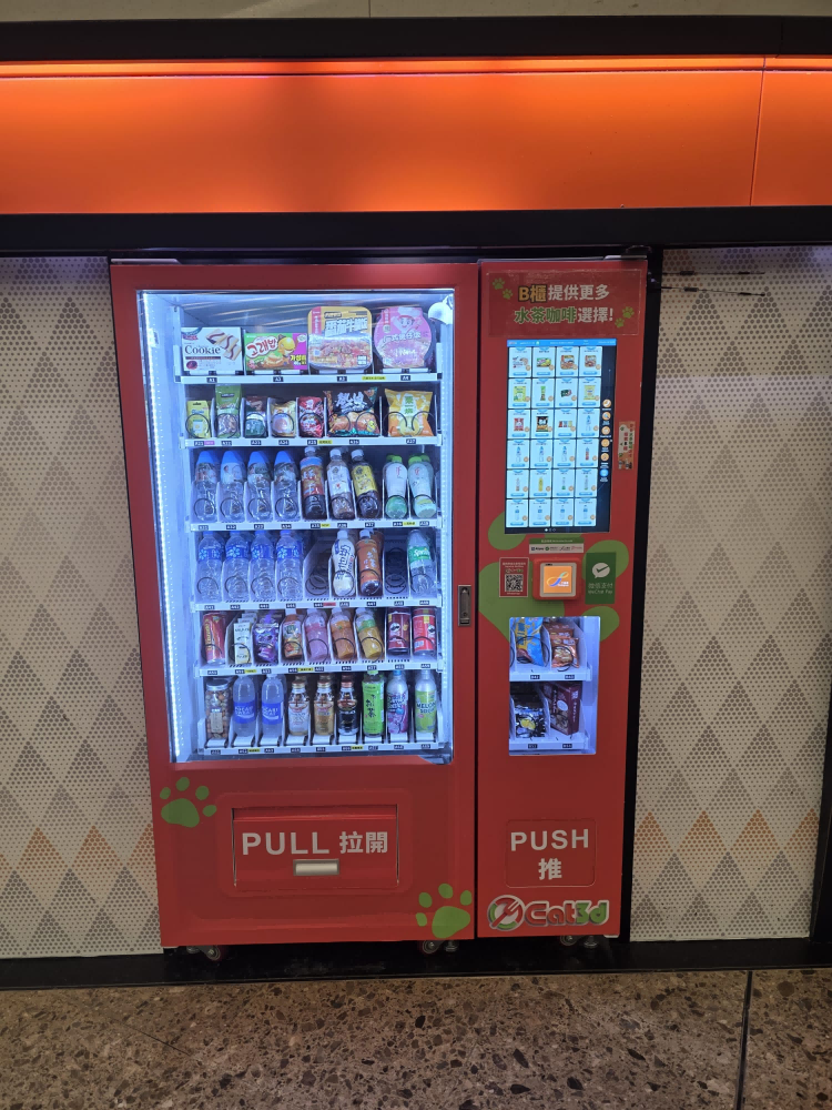 Dual-zone refrigerated snack vending machine dispensing drinks and packaged snacks in a Hong Kong high-speed rail station concourse