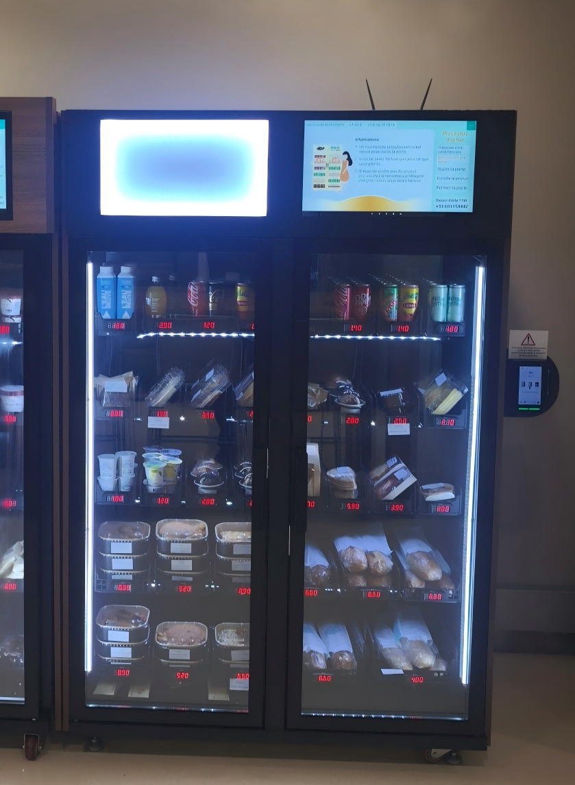 Weight-sensing smart fridge food vending machine dispensing fresh sandwich and boxed meal options in a French corporate lounge