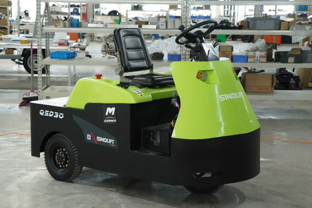 Rider-seated electric towing tractor (QSD30/QSD60) hauling heavy loads in large distribution center for long-distance material handling