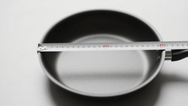 Measure a pan by placing it flat on a surface and measuring straight across the top from one rim to the other Measure a pan by placing it flat on a surface and measuring straight across the top from one rim to the other