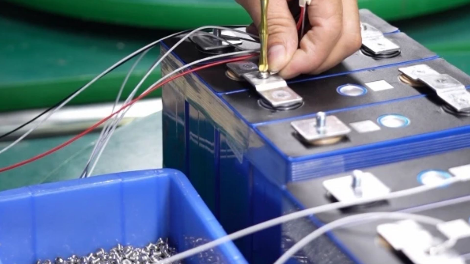 Technician connecting test and BMS sense leads to the bolt terminals of blue rectangular prismatic LiFePO4 cells during sample and small-batch inspection