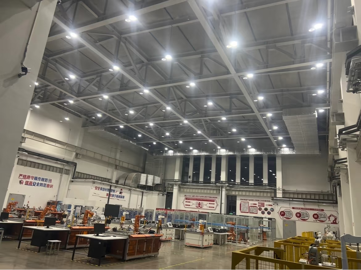 Lumin UFO LED high bay light installed in a large warehouse with high rack shelving, illuminating aisles with uniform 120-degree beam distribution.