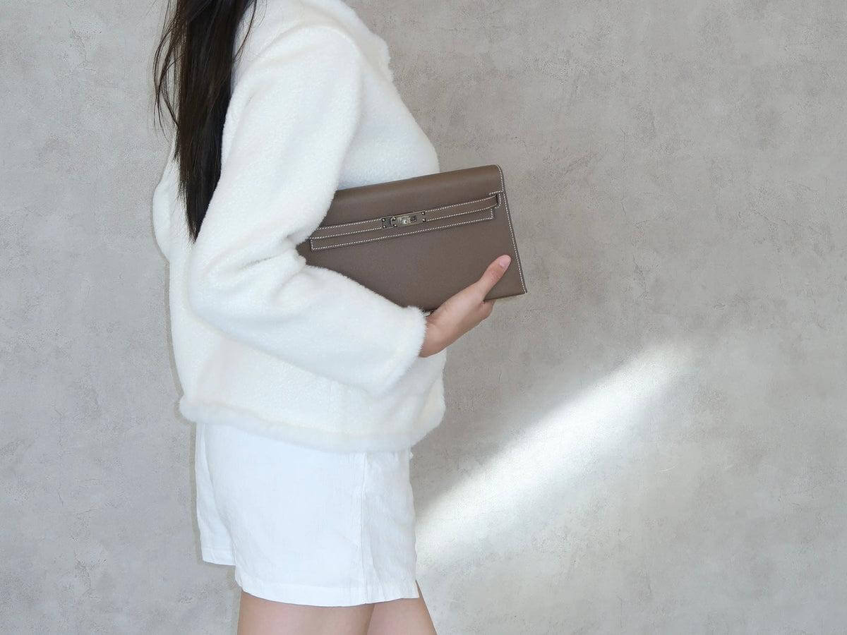 A woman holding a clutches bag with one hand to show its size and grip.