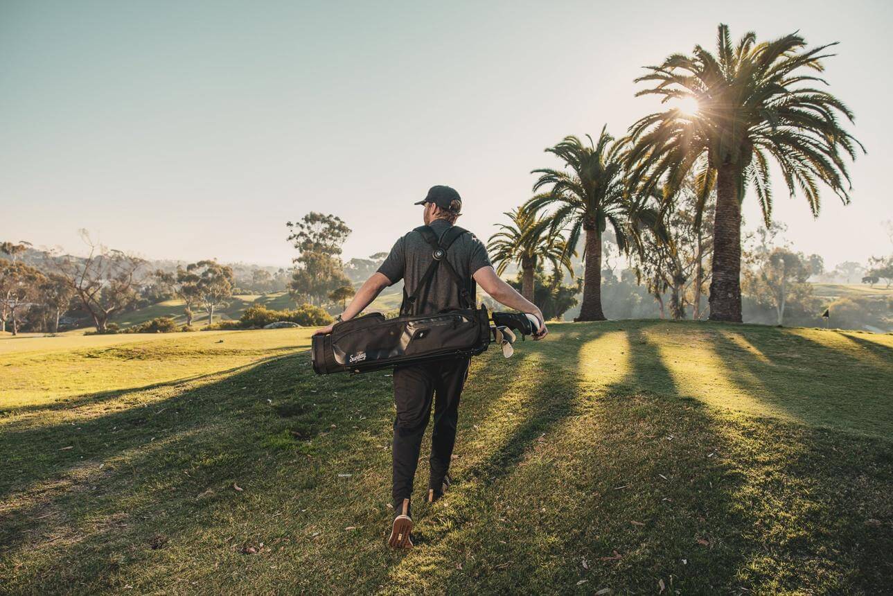 A golfer carrying a lightweight golf bag on a lush green course, natural lighting