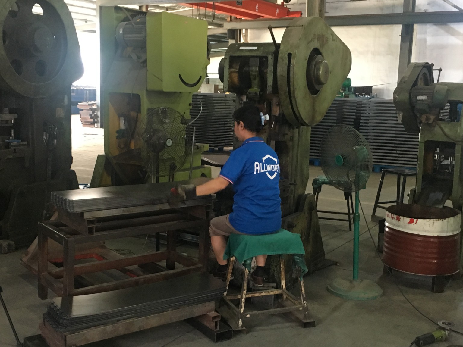 ALLWORTH worker handling metal components beside a press in the factory workshop