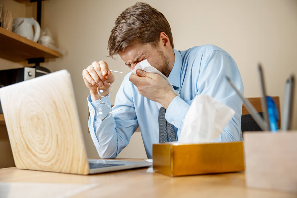 A man suffering from rhinitis at his desk