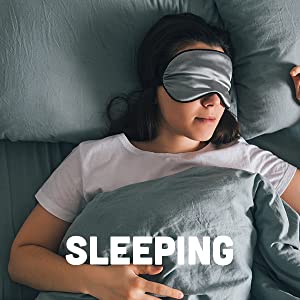 White woman in a white tee shirt sleeping on a bed with gray linens and a sleeping mask