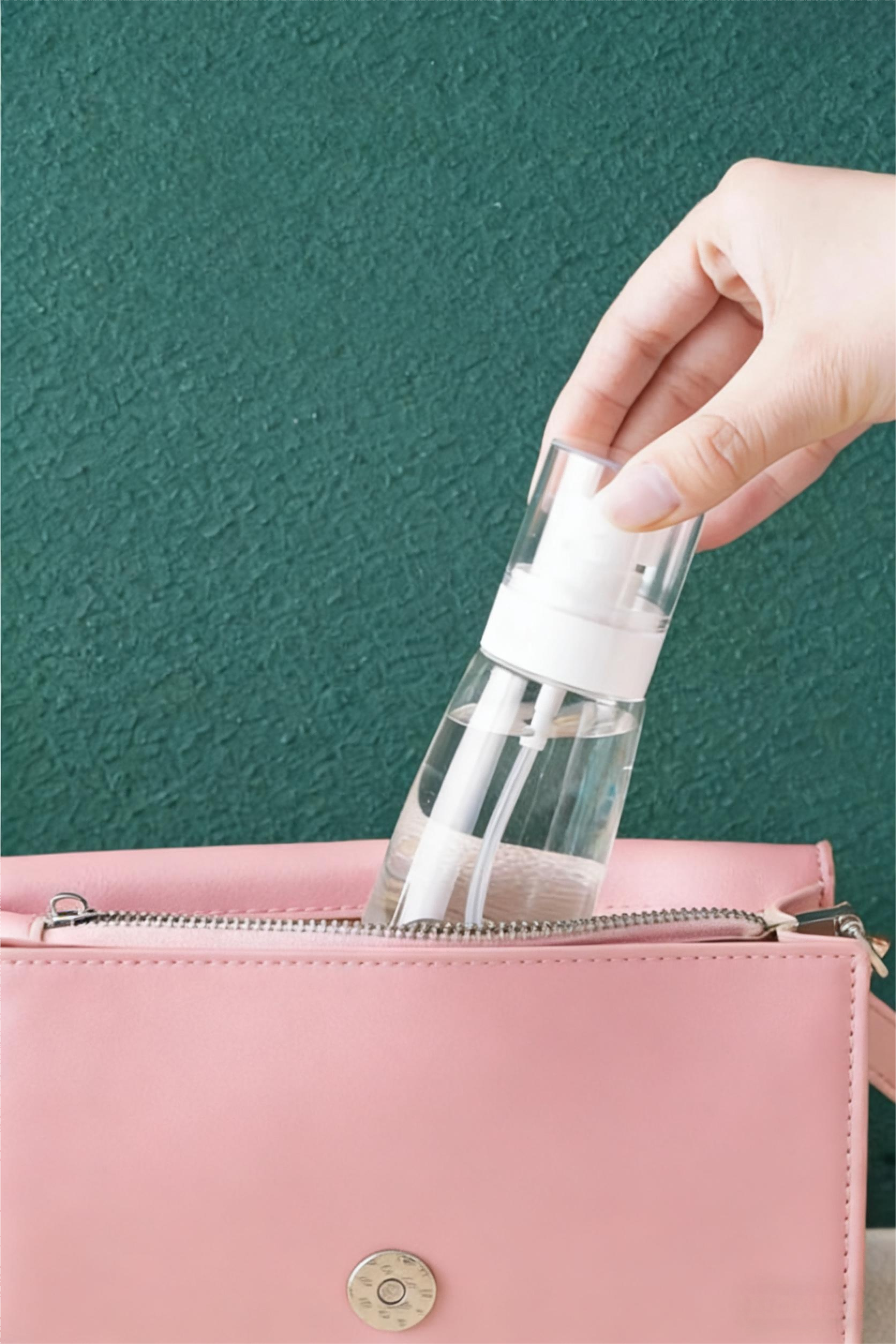 A hand taking a clear travel-sized spray bottle out of a pink handbag, demonstrating its compact, portable size