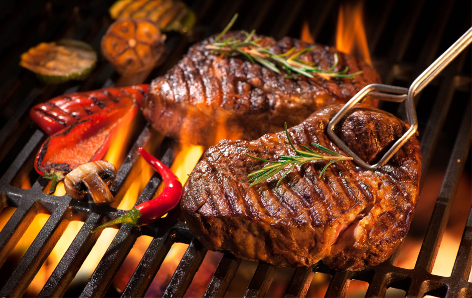 Juicy seared steaks with rosemary and vegetables on a flaming gas grill, visual guide for how to grill steak on gas grill