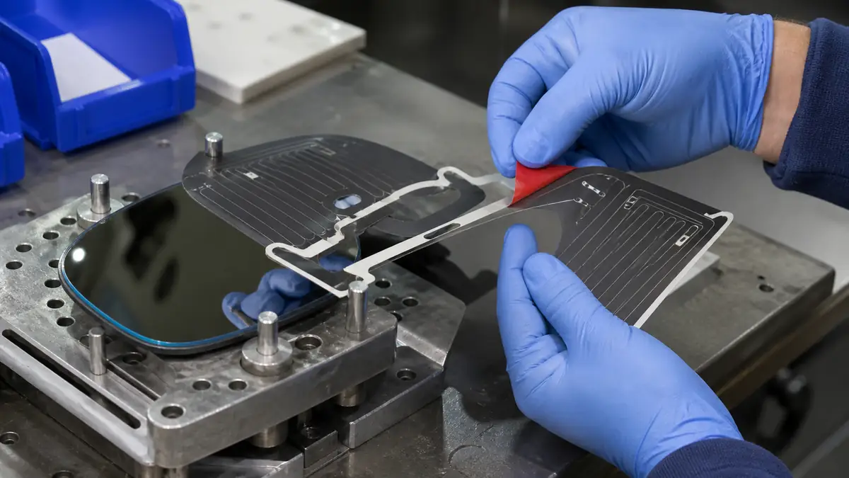 Technician peeling a red liner from custom die-cut tape while aligning an automotive mirror heater pad