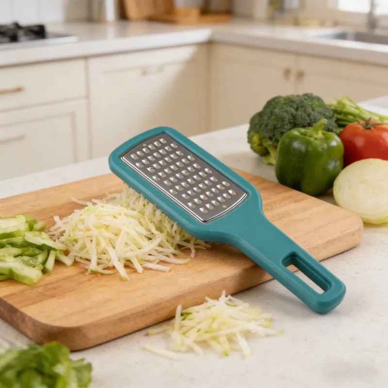 Teal hand grater with stainless steel grating surface resting on a wooden cutting board, with shredded vegetables and fresh produce in a bright modern kitchen.