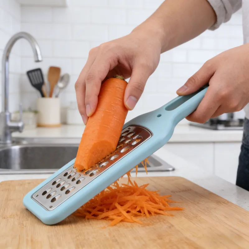 Light blue hand grater with stainless steel blade being used to shred a fresh carrot on a wooden cutting board in a bright kitchen, with shredded carrots falling below.
