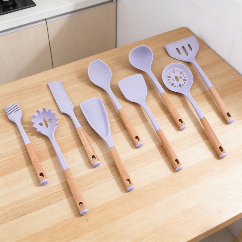 10-piece light purple silicone kitchen utensil set with wooden handles, neatly arranged on a light wood kitchen countertop, including spatulas, spoons, slotted turner, pasta fork, skimmer, basting brush, and knife.