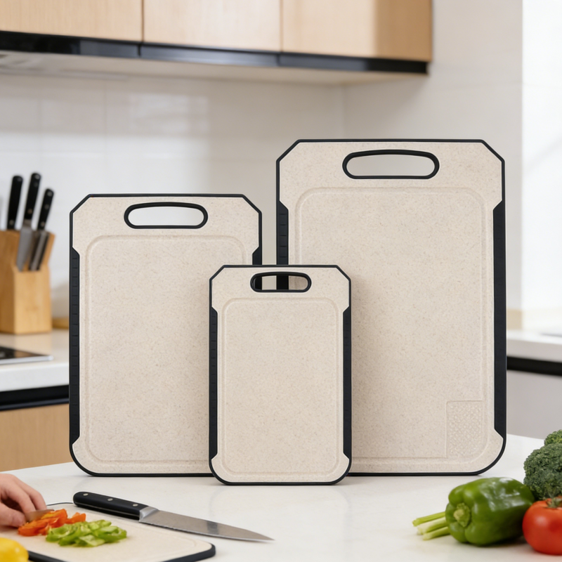 Three-piece set of wheat-straw kitchen cutting boards in small, medium, and large sizes, with black non-slip edges, hanging handles, and a juice groove, displayed on a clean countertop alongside fresh vegetables and a person chopping peppers in a bright modern kitchen.