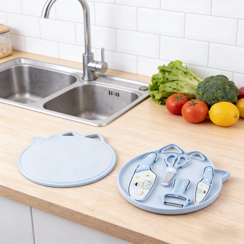 Cute light blue cat-shaped kitchen utensil set with cutting board, knives, scissors and peeler placed on a wooden countertop in a bright modern kitchen.