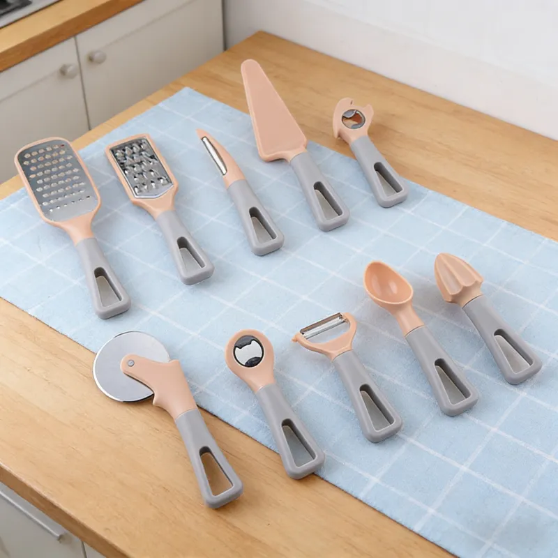 Set of 11 peach and gray kitchen gadgets (graters, fruit knife, cake server, bottle openers, pizza cutter, peeler, spoon, citrus juicer) neatly arranged on a light blue checkered towel over a wooden kitchen countertop.