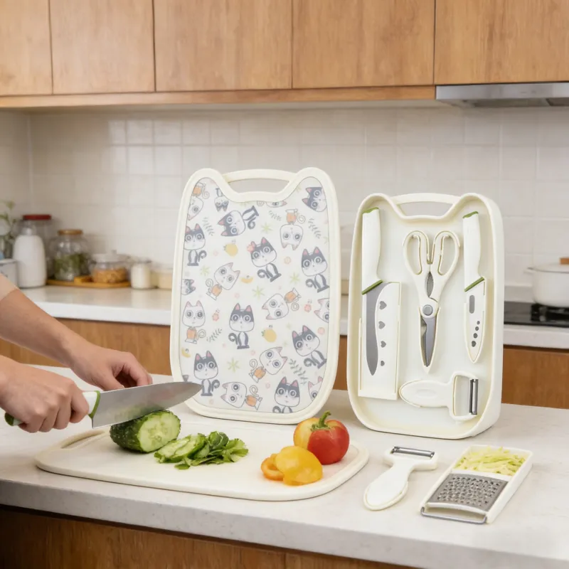 A cat-patterned kitchen tool set (including a cutting board, knives, scissors, and a peeler) is displayed in a bright kitchen, with hands slicing cucumber on a plain white cutting board, surrounded by fresh vegetables and kitchen utensils.