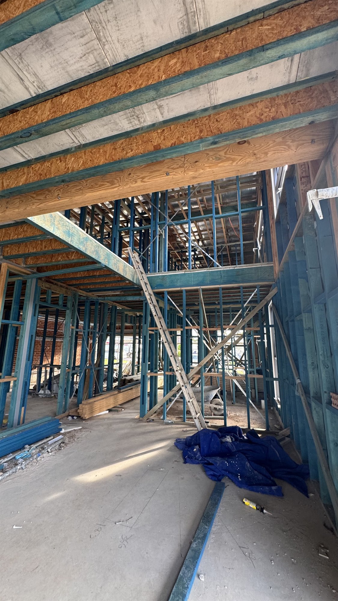 Stair opening in a Sydney house under construction, blue framing and timber joists above a concrete slab