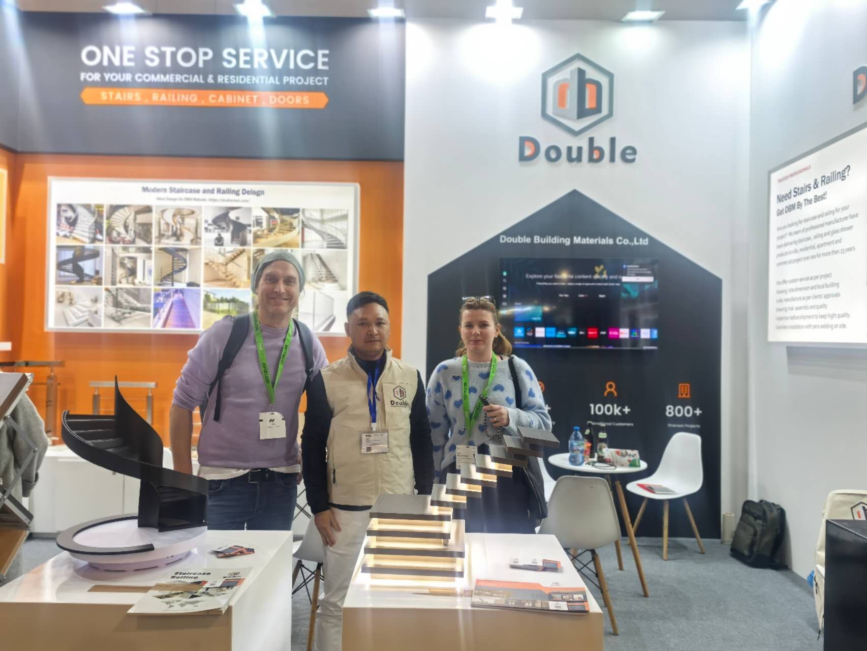 Staff and two visitors at stand 443 beside a black spiral staircase model and a lit step sample