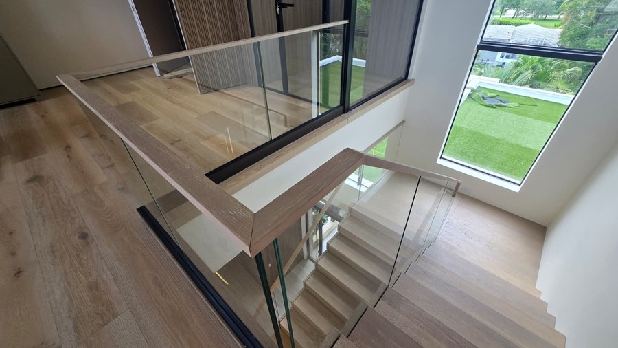Looking down stacked white oak flights with frameless glass balustrade toward a Florida lawn