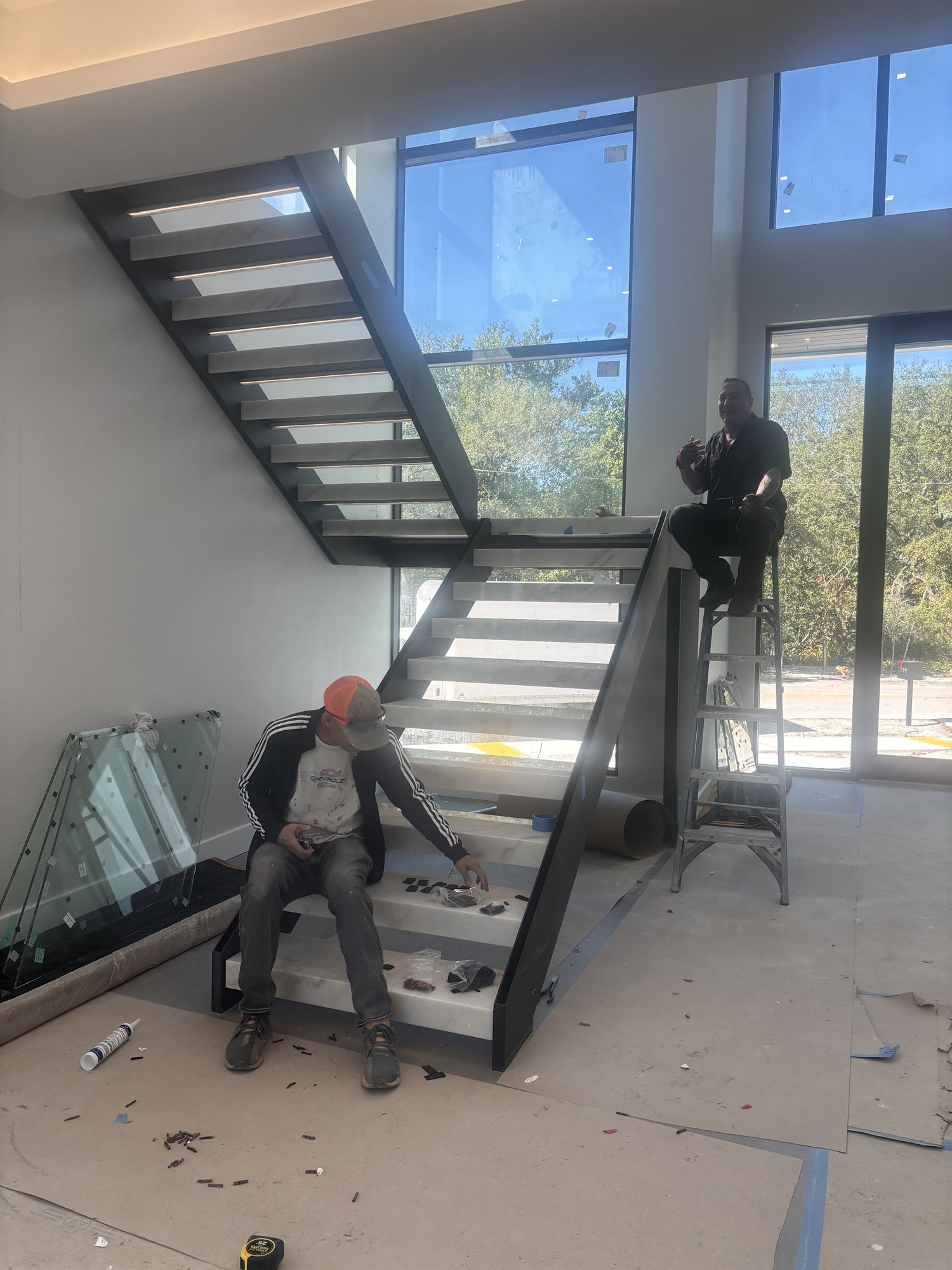 Local crew fitting a black-stringer stone staircase with glass panels still in wrap