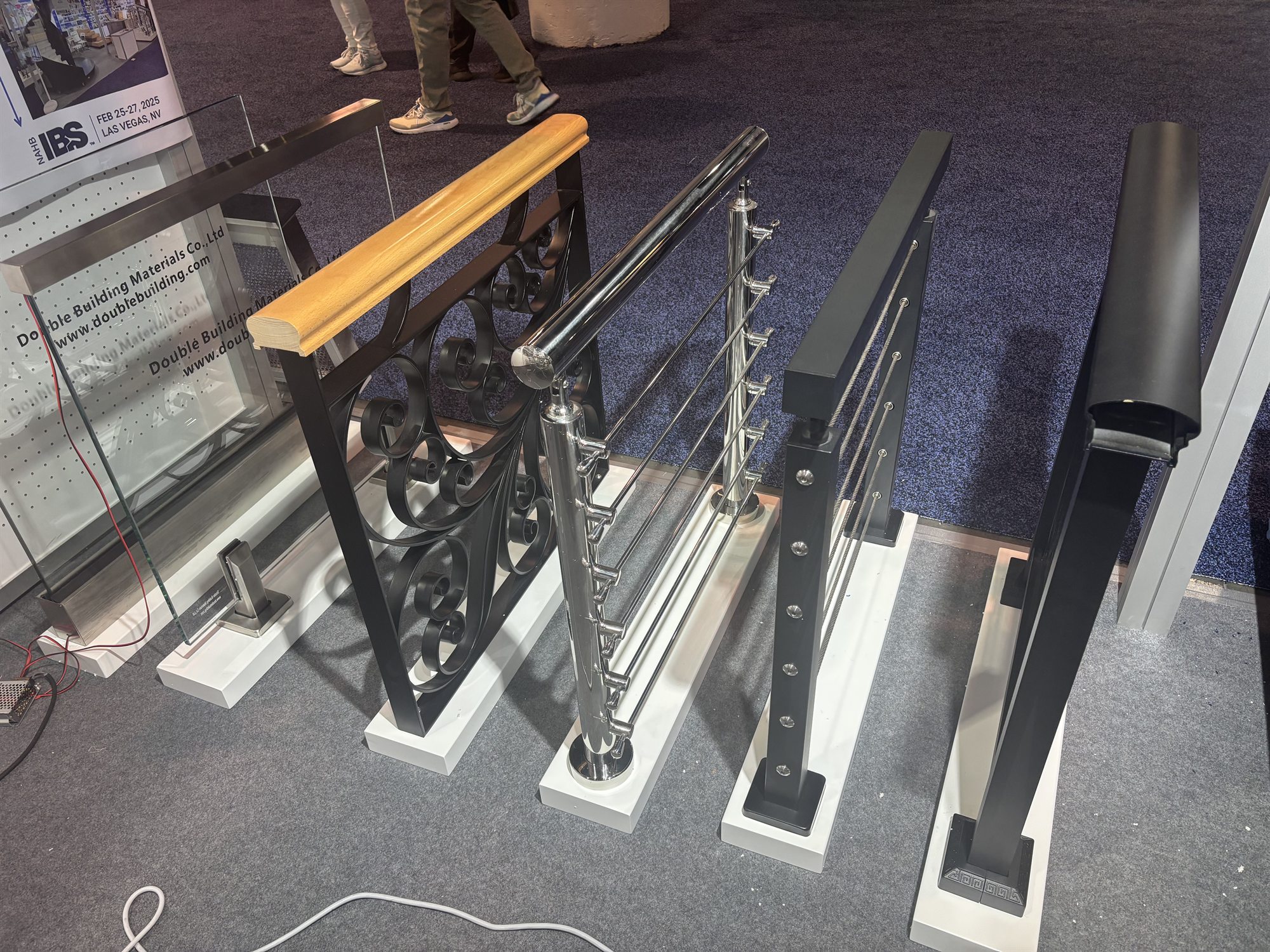 Five railing post samples in a line at IBS 2025, including glass railing, cable, and wood-topped iron