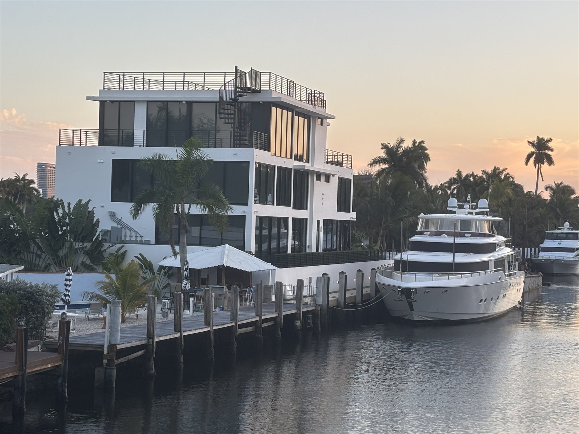 White canal house at dusk with black cable railing on the balconies and a yacht at the dock