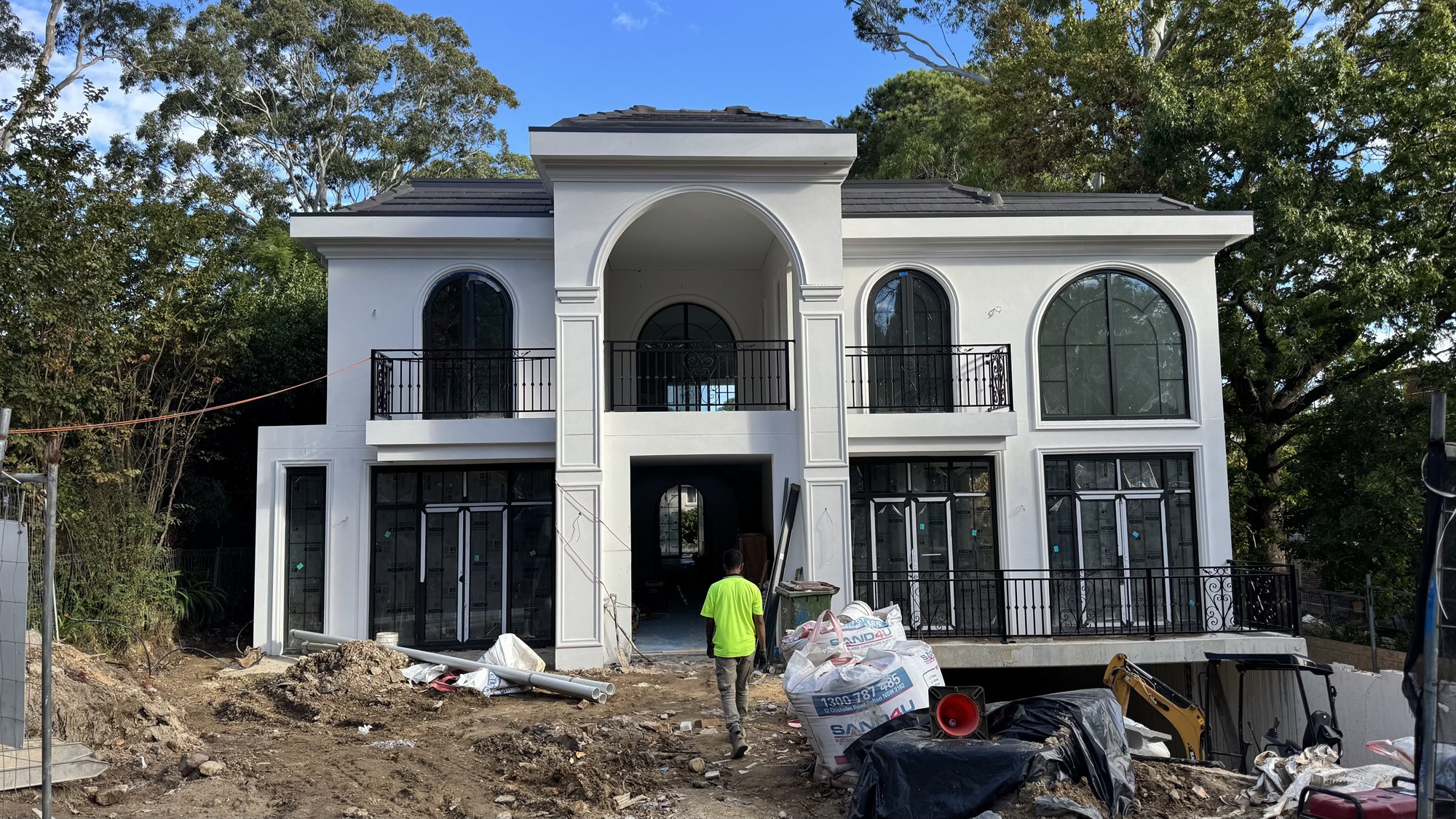 White two-storey Sydney house under construction with arched windows and sand bags in the yard