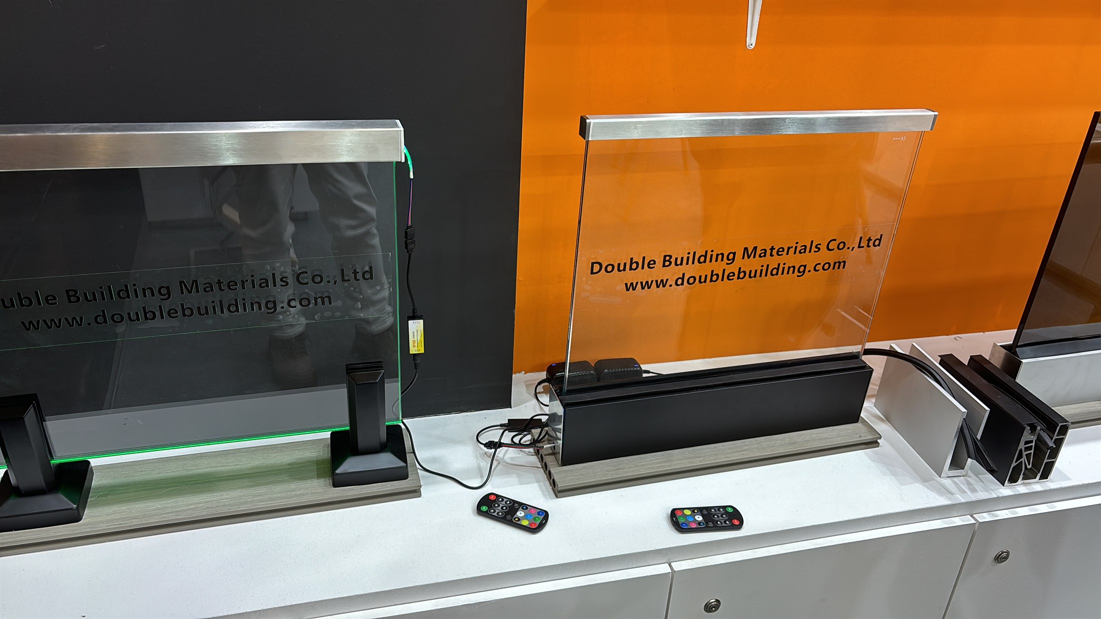 Two glass railing samples on the BAU 2025 counter, one in base posts with light and one in a channel, with remotes