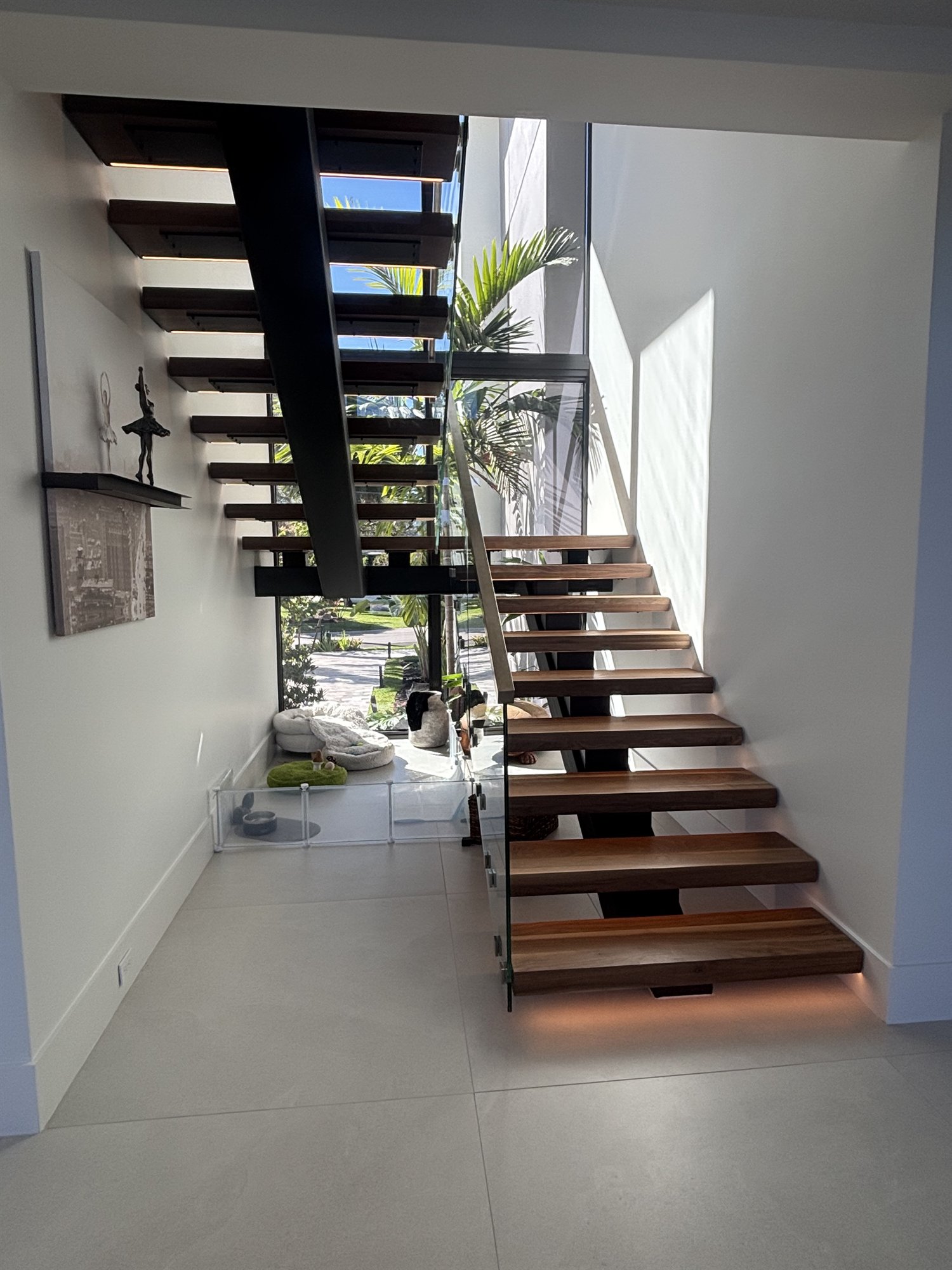 Walnut-toned floating staircase with black steel spine, glass railing and under-tread light