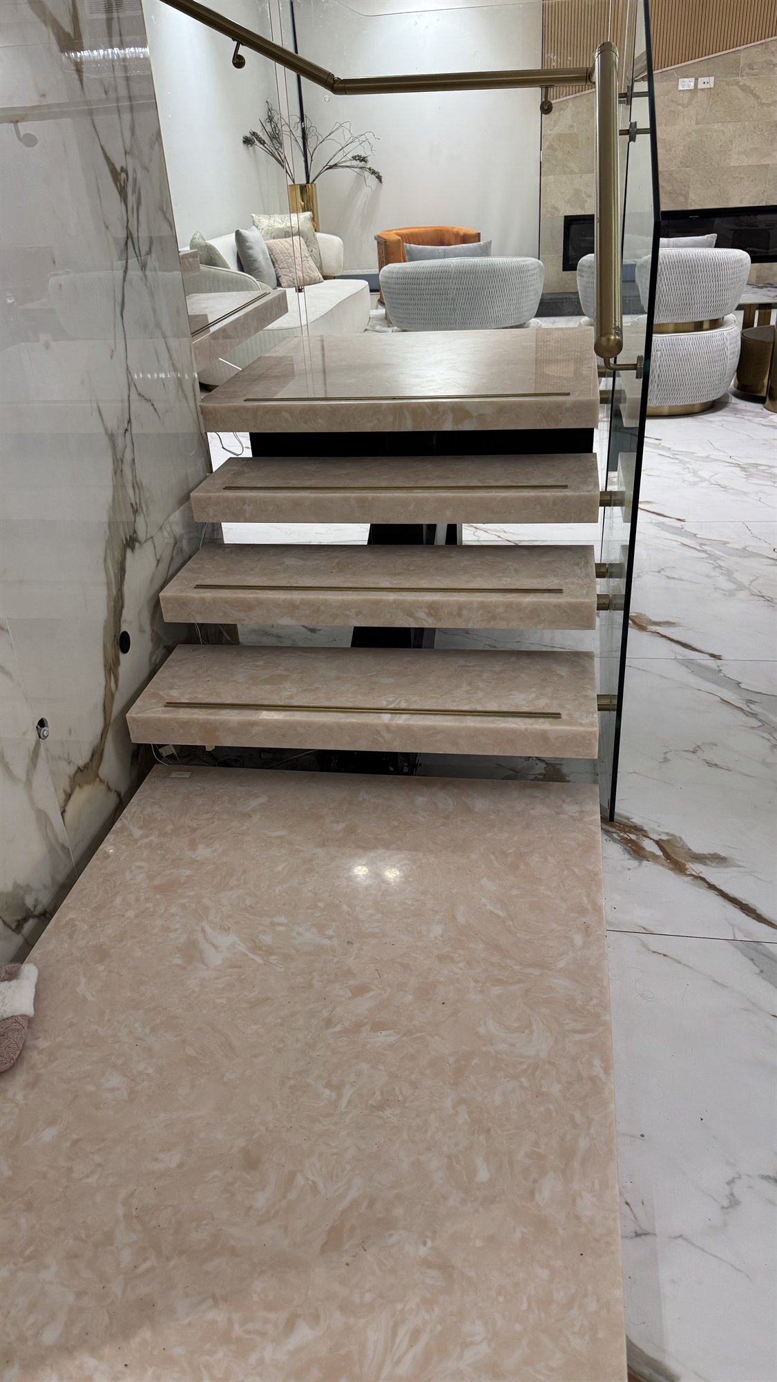 Finished pale marble floating staircase with glass panels, a dark steel spine and a brass handrail in a Sydney home