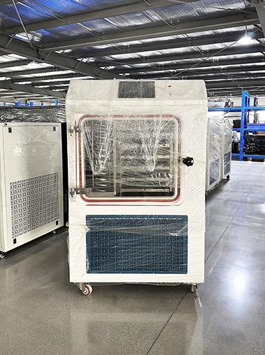 Front view of an industrial lyophilizer machine covered in clear protective wrap on a factory workshop floor.