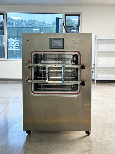 Straight front view real shot of an industrial freeze dryer machine in a bright factory room, highlighting its upper digital touch screen and large observation window with sealing red ring.