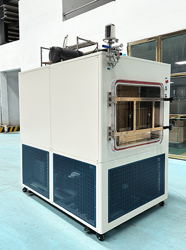 Front view of a professional industrial freeze dryer in a factory setting, featuring a high-visibility square chamber door and a sturdy blue cooling ventilation base.