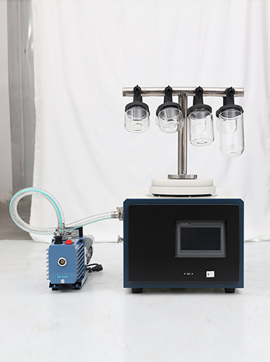 Front view of Geliss benchtop vacuum freeze dryer with a stainless steel T-shaped manifold rack and glass bottles, hooked up to an external vacuum pump.