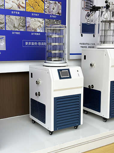 Right angled showroom view of an ordinary laboratory freeze dryer featuring a transparent acrylic vacuum cover, positioned next to another unit against a product poster background.