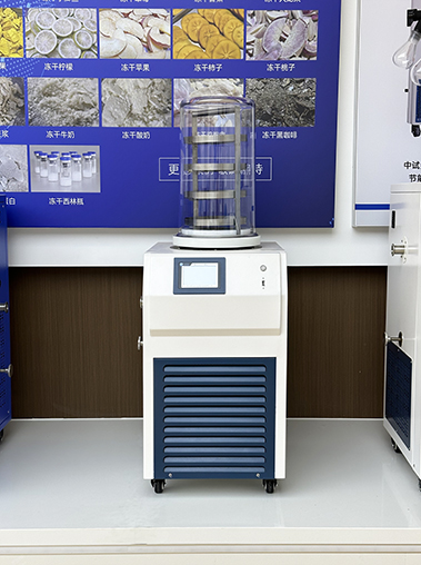 Front showroom view of an ordinary vacuum freeze dryer with a clear acrylic drying chamber and sample shelves, displayed under a colorful product application poster.