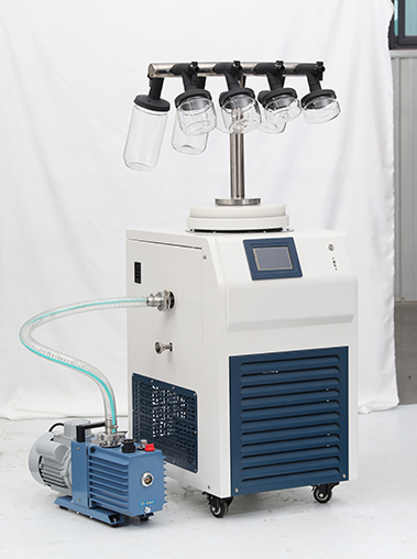 Front view real shot of a T-frame laboratory freeze dryer equipped with clear wide-mouth glass bottles and connected to a blue vacuum pump.