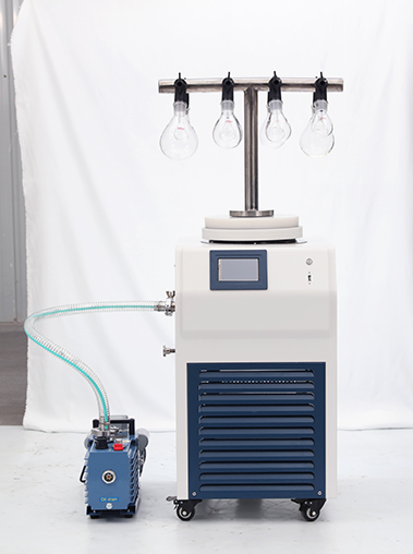 Angled workshop shot of a vacuum freeze dryer with an eggplant flask T-frame manifold linked to a blue vacuum pump via a transparent reinforced hose.