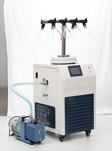 Front view real shot of a laboratory freeze dryer with an eggplant flask T-frame manifold connected to a blue rotary vane vacuum pump on a white backdrop.