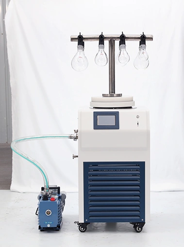 Angled workshop shot of a vacuum freeze dryer with an eggplant flask T-frame manifold linked to a blue vacuum pump via a transparent reinforced hose.