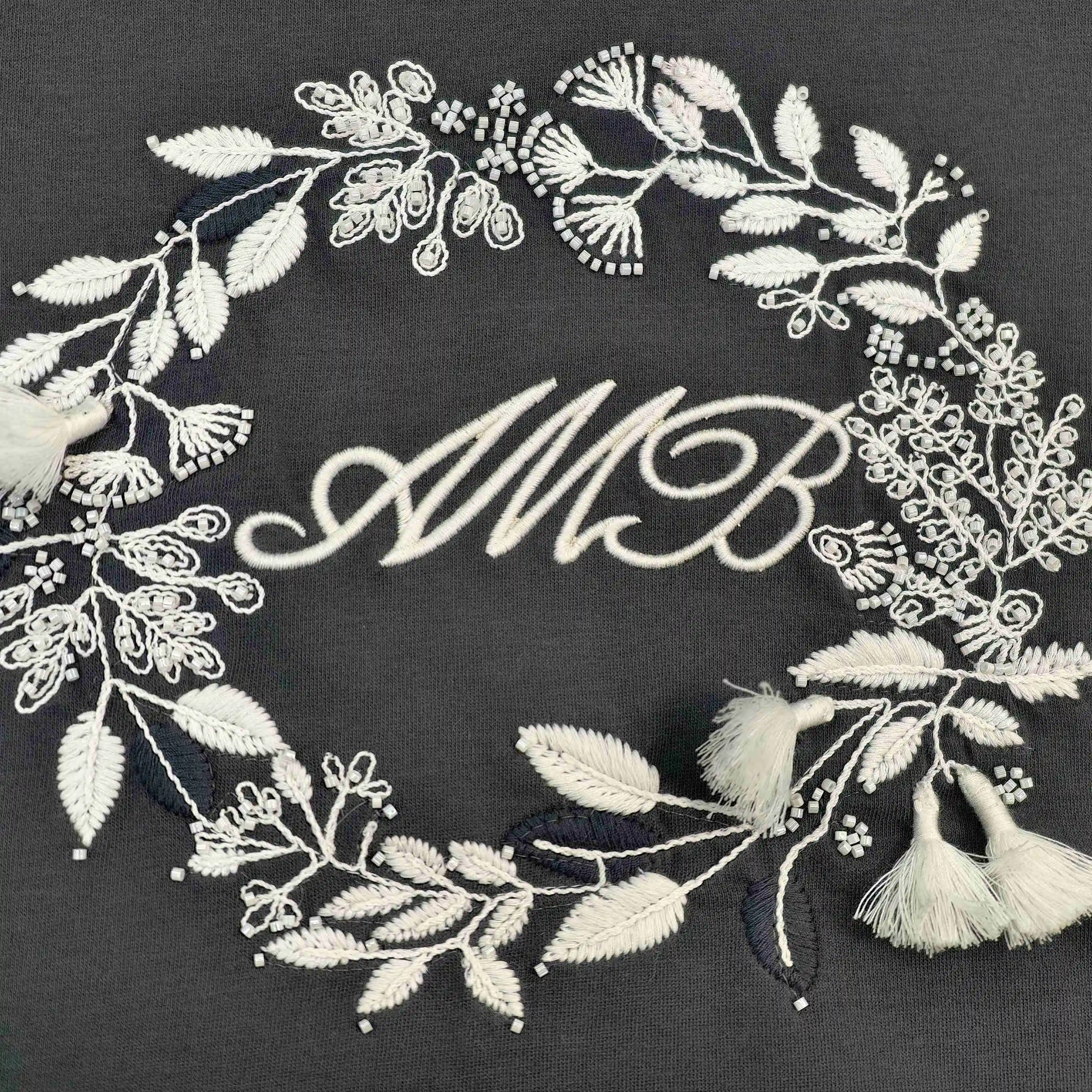 Cream floral wreath embroidery with monogram and tassel details